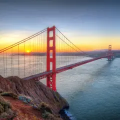 Zachód słońca nad Zatoką San Francisco, gdzie majestatyczny san francisco most rozciąga się nad wodą, a jego czerwone wieże lśnią w złotym świetle.