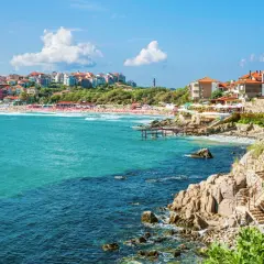 Słoneczne wybrzeże z turkusowym morzem, plażą pełną ludzi i kolorowymi budynkami na wzgórzu – tak z czego słynie Bułgaria.