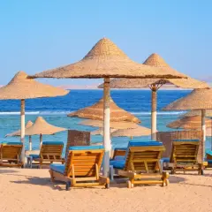 Plaża z leżakami i parasolami, idealne miejsce na tanie kierunki na wakacje. Błękitne morze i góry w tle.