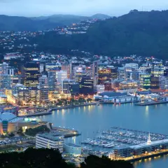 Wellington, stolica Nowej Zelandii, nocą. Miasto rozświetlone tysiącami świateł, z górami w tle i zatoką pełną jachtów.