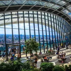 Relaks w Sky Garden w Londynie. Ludzie odpoczywają wśród zieleni, podziwiając panoramę miasta przez szklany dach.