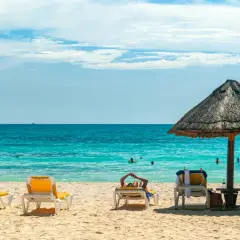 Idealne miejsce, gdzie na wakacje we wrześniu: pusta plaża z leżakami i parasolem, turkusowe morze i błękitne niebo.