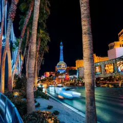 Nocne Las Vegas atrakcje: palmy, neonowe światła, wieża Eiffla i ruch uliczny.