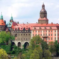 Imponujące zamki w okolicy Wrocławia, z wieżami i czerwonymi dachami, otoczone zielenią.