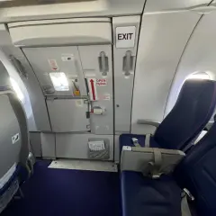 Wnętrze samolotu Wizzair. Widok na rząd siedzeń i drzwi wyjściowe. Numeracja miejsc w samolocie Wizzair jest widoczna na siedzeniach.