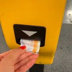 Dłoń z czerwoną hybrydą wkłada bilet do żółtego automatu. Praga komunikacja miejska - kupno biletu.