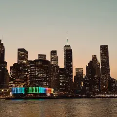 Wieczorny widok na Manhattan podczas zwiedzania Nowego Jorku. Podświetlone wieżowce odbijają się w wodzie.