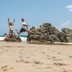 Szczęśliwa para skacze na plaży w meksykańskim kurorcie nad Pacyfikiem, z falami i skałami w tle.