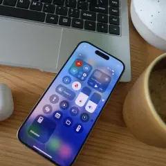 Na ekranie iPhone'a widać centrum sterowania, gdzie łatwo włączyć tryb samolotowy, dotykając ikony samolotu. Obok leży laptop i kubek kawy.
