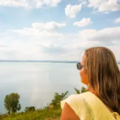 Kobieta w żółtej bluzce patrzy na rozległe jezioro, zastanawiając się, gdzie nad Balaton.