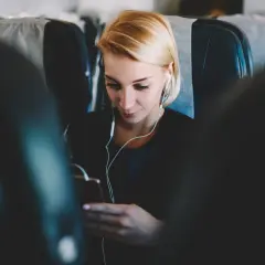 Kobieta w słuchawkach korzysta z telefonu, ciesząc się internetem w samolocie.