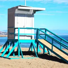 Ratownik na plaży w Fuengiroli, jedna z atrakcji Costa del Sol. Błękitna konstrukcja i biała budka ratownicza na tle morza i gór.