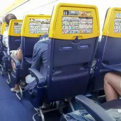Wnętrze samolotu Ryanair. Widok na rząd siedzeń z żółtymi zagłówkami i instrukcjami bezpieczeństwa. Numeracja miejsc w samolocie Ryanair jest widoczna.