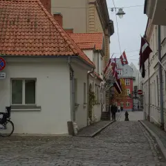 Urokliwa uliczka w Rydze, z łotewskimi flagami i brukowaną nawierzchnią. Idealne miejsce, by poczuć atmosferę miasta i zobaczyć, co zobaczyć w Rydze.