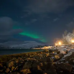 Nocne niebo nad Tromsø, kiedy zorza tańczy na tle ośnieżonych gór.