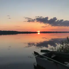 Łódź czeka nad spokojną rzeką białych nocy, odbijając pomarańczowe niebo i chmury.
