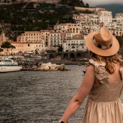 Kobieta w kapeluszu podziwia malownicze widoki Amalfi. Warto zobaczyć to miasto pełne urokliwych domków i portu z łodziami.