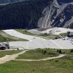 Alpejskie lotnisko, jedno z najniebezpieczniejszych lotnisk w Europie, z samolotami na pasie startowym i budynkami w otoczeniu gór.