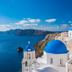 Santorini, idealne miejsce, gdzie na wakacje w sierpniu. Białe domy z niebieskimi kopułami nad lazurowym morzem.