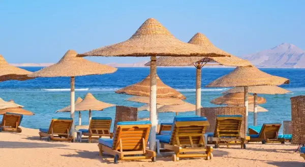 Plaża z leżakami i parasolami, idealne miejsce na tanie kierunki na wakacje. Błękitne morze i góry w tle.