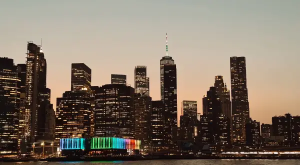 Wieczorny widok na Manhattan podczas zwiedzania Nowego Jorku. Podświetlone wieżowce odbijają się w wodzie.