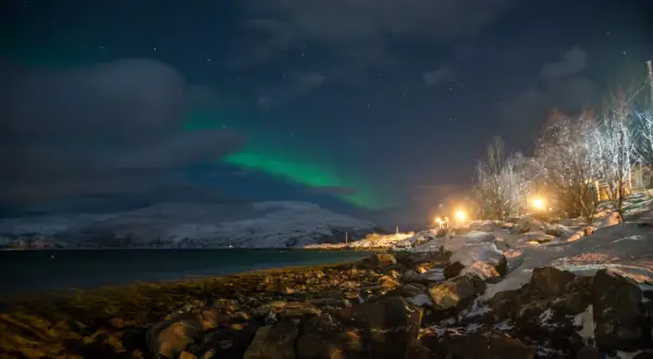 Nocne niebo nad Tromsø, kiedy zorza tańczy na tle ośnieżonych gór.