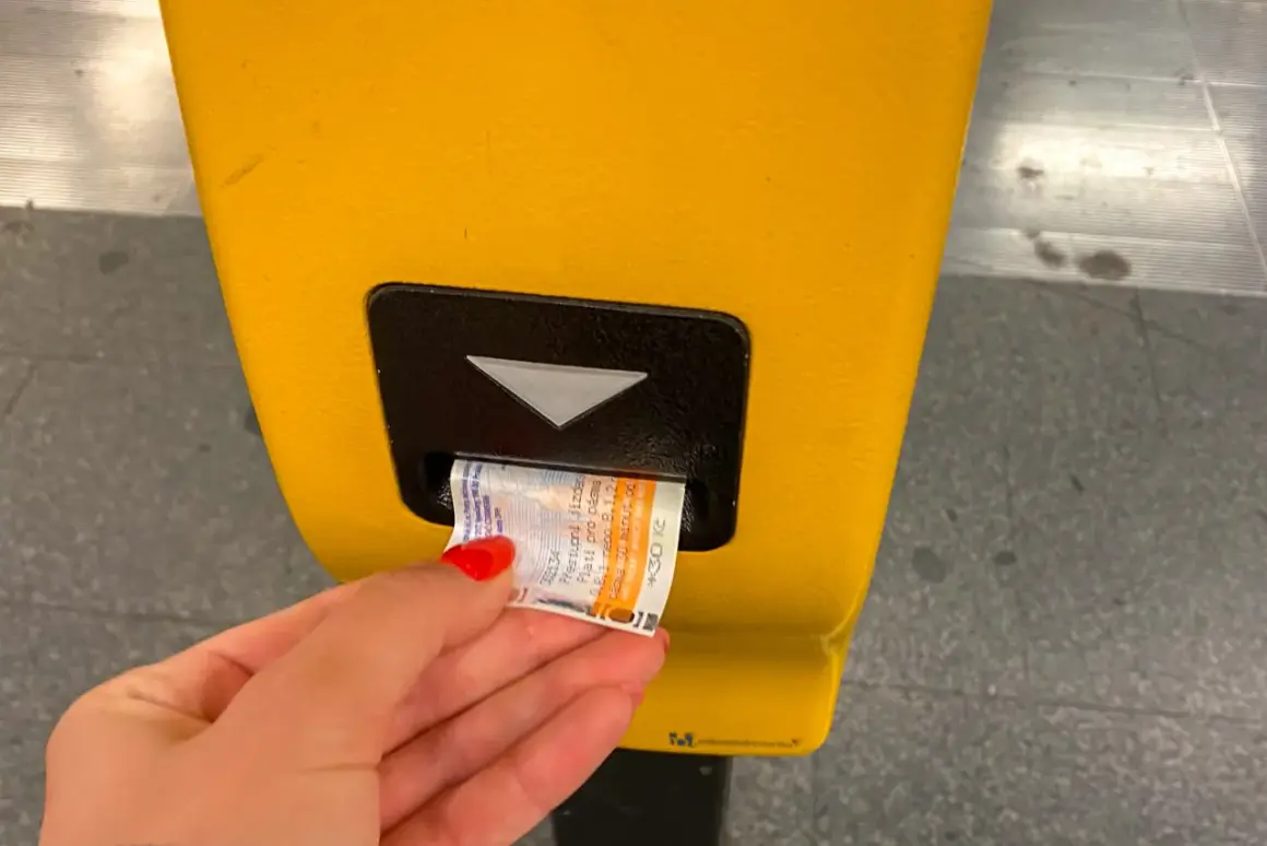Dłoń z czerwoną hybrydą wkłada bilet do żółtego automatu. Praga komunikacja miejska - kupno biletu.