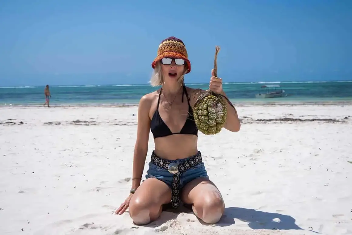 Kobieta w bikini i kapeluszu na plaży z egzotycznym owocem. Idealne miejsce na wakacje, by odkrywać nowe smaki.