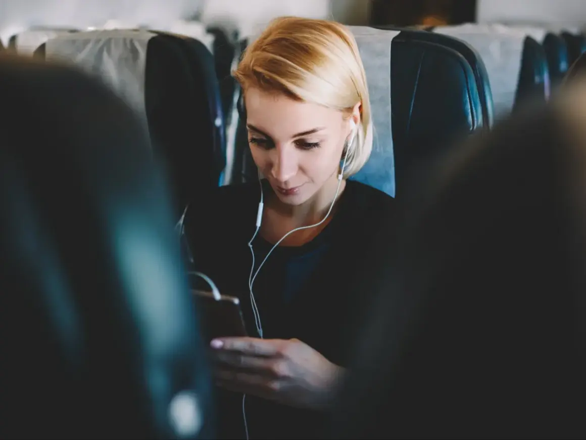Kobieta w słuchawkach korzysta z telefonu, ciesząc się internetem w samolocie.