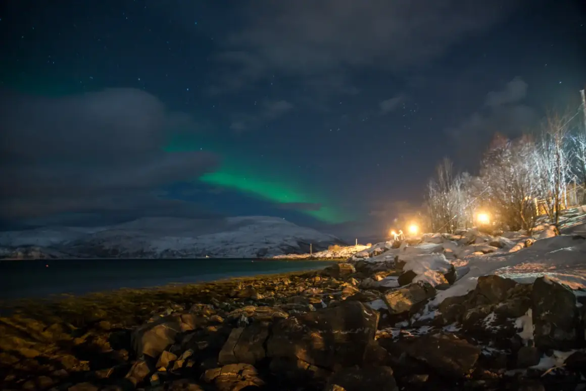 Nocne niebo nad Tromsø, kiedy zorza tańczy na tle ośnieżonych gór.