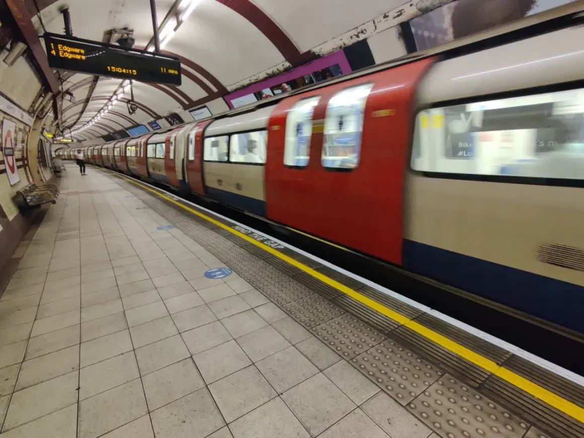 Metro londyn bilet 3 dniowy. Pociąg z czerwonymi i beżowymi elementami mija peron. Na tablicy informacja o odjeździe do Edgware.