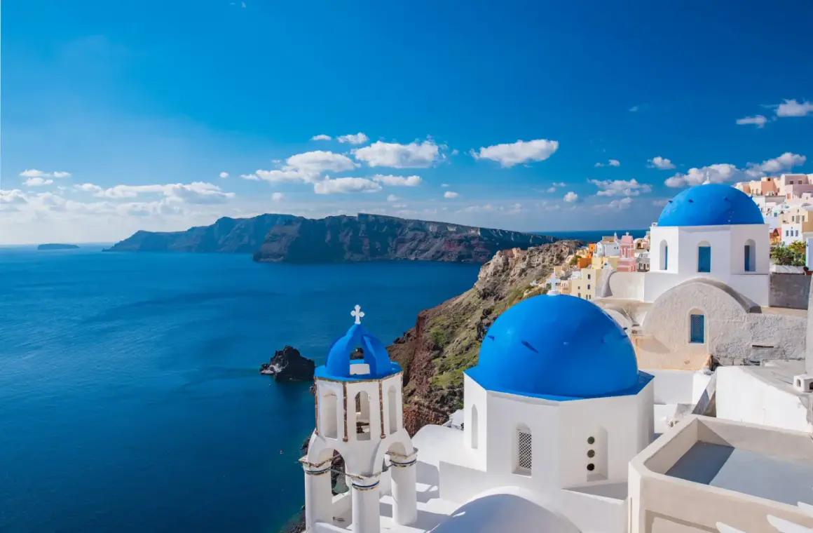 Santorini, idealne miejsce, gdzie na wakacje w sierpniu. Białe domy z niebieskimi kopułami nad lazurowym morzem.