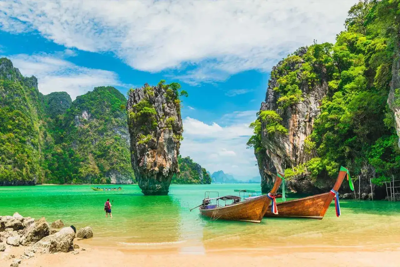 Piękne, zielone skały wyrastające z turkusowej wody, łodzie i plaża. Idealne miejsce na wakacje, zastanawiasz się phuket kiedy jechać?