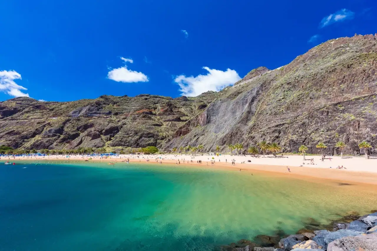 Idealne miejsce, gdzie na wakacje w czerwcu: piaszczysta plaża, turkusowa woda i skaliste góry w tle.