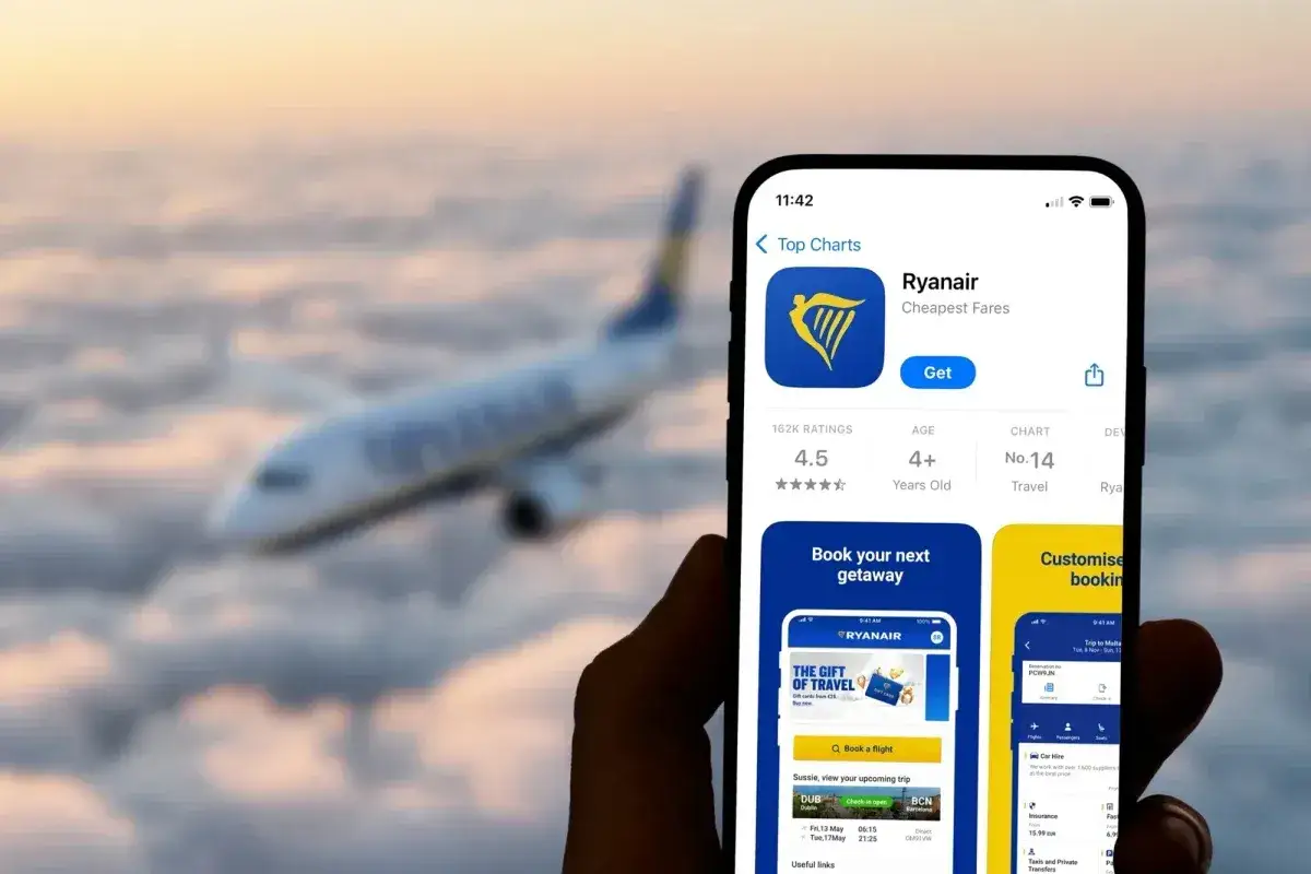 Ręka trzyma smartfon z aplikacją Ryanair, gotową do odprawy online. W tle widać samolot lecący nad chmurami.