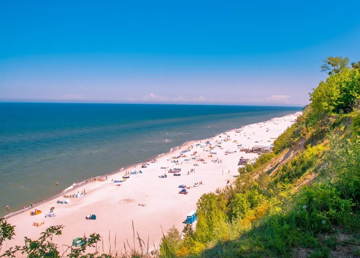 Słoneczna plaża pełna ludzi, idealna na letni wypoczynek w miejscowościach blisko Trójmiasta.