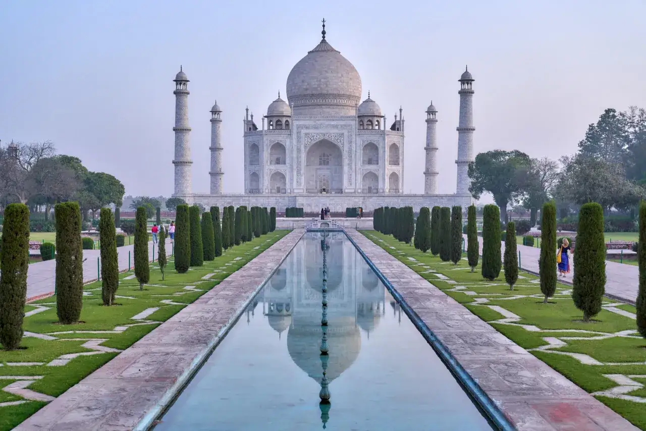 Majestatyczny Taj Mahal w Indiach odbija się w spokojnej wodzie, otoczony geometrycznymi ogrodami i strzelistymi cyprysami.
